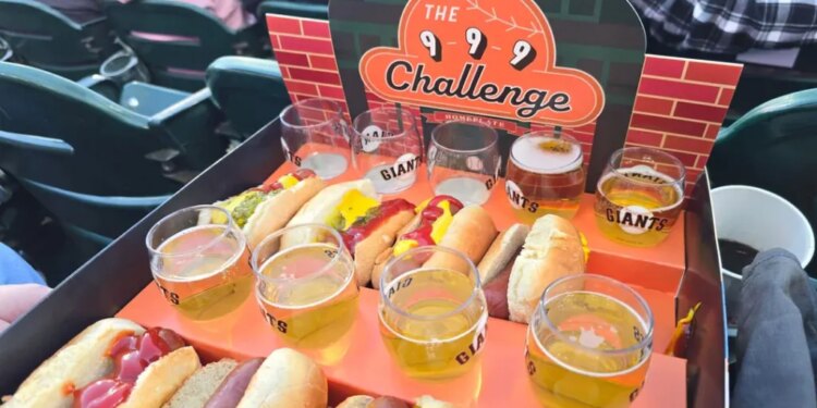A tray of 9 small beers and 9 hot dogs at a baseball stadium with "The 9-9-9 Challenge" sign.