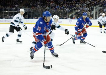 New York Rangers players in blue jerseys facing off against Utah Mammoth players in white jerseys during a hockey game.