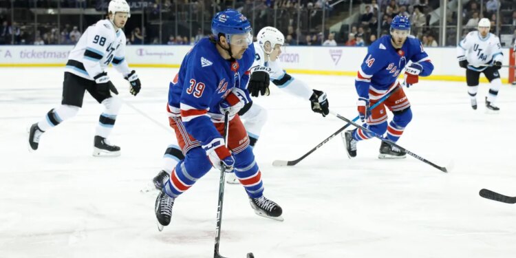 New York Rangers players in blue jerseys facing off against Utah Mammoth players in white jerseys during a hockey game.