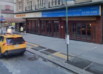 A yellow taxi on a city street in front of a building with a "For Lease or Sale" sign.