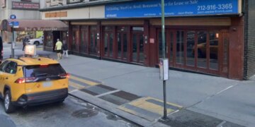 A yellow taxi on a city street in front of a building with a "For Lease or Sale" sign.