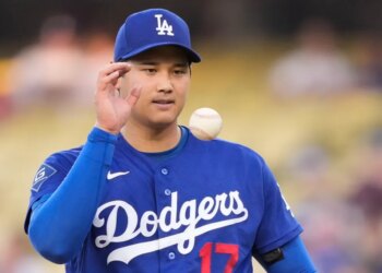Shohei Ohtani in a Dodgers uniform with a baseball on his shoulder.
