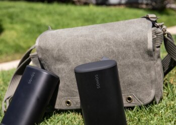 Two Sonos Play speakers in front of a sage colored bag on the grass.