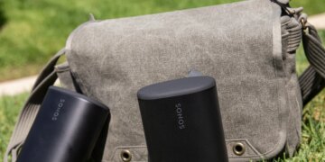 Two Sonos Play speakers in front of a sage colored bag on the grass.