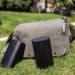 Two Sonos Play speakers in front of a sage colored bag on the grass.