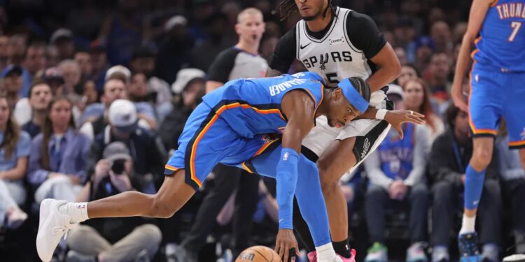 Oklahoma City Thunder guard Shai Gilgeous-Alexander, center, tries to keep control of the ball against San Antonio Spurs guard Stephon Castle (5).