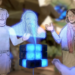 A still from a stop-motion animation depicting two adults and a child made of paper who are marveling at a hologram being projected from a glowing, Rubik’s cube-like object.