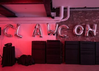 An image of a room with pink lighting and silver balloons spelling out CLAWCON.