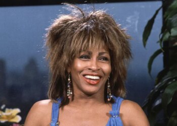 Tina Turner smiling with her mouth open, wearing a blue top and beaded earrings.