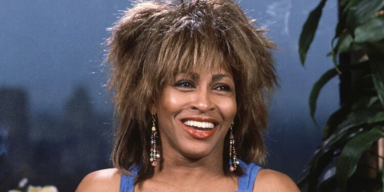 Tina Turner smiling with her mouth open, wearing a blue top and beaded earrings.