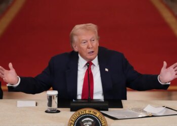 President Donald Trump speaking at a roundtable discussion on college sports, with his arms outstretched.
