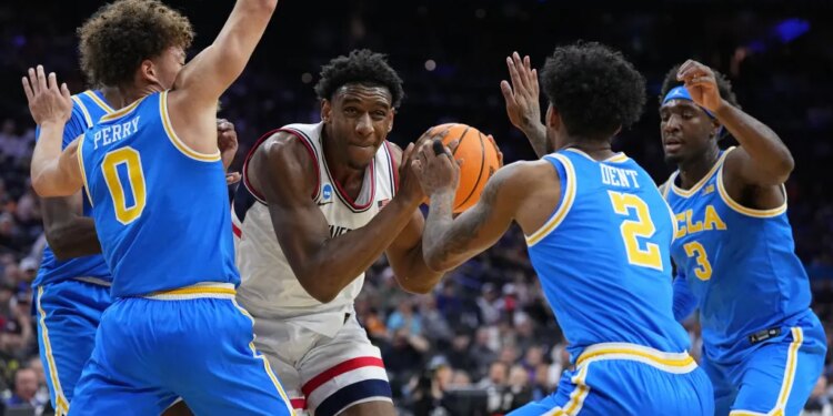 UConn's Tarris Reed Jr. holding the basketball, surrounded by UCLA players Trent Perry, Donovan Dent, and Eric Dailey Jr.