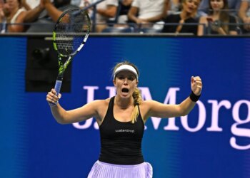 A female tennis player in a black top and light purple skirt, holding a tennis racket and celebrating a point with both arms raised.