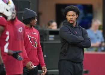 Injured Arizona Cardinals quarterback Kyler Murray, right, looks on as teammates warm up.