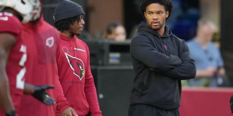 Injured Arizona Cardinals quarterback Kyler Murray, right, looks on as teammates warm up.