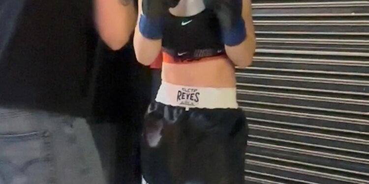 A boxer, with braids and boxing gloves, faces another person who is only partially visible.