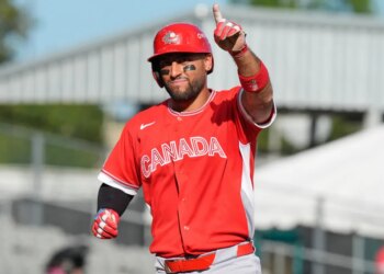 Abraham Toro, wearing a red "CANADA" jersey, red helmet, and eye black, points his right index finger upwards while celebrating during a baseball game.