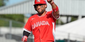 Abraham Toro, wearing a red "CANADA" jersey, red helmet, and eye black, points his right index finger upwards while celebrating during a baseball game.