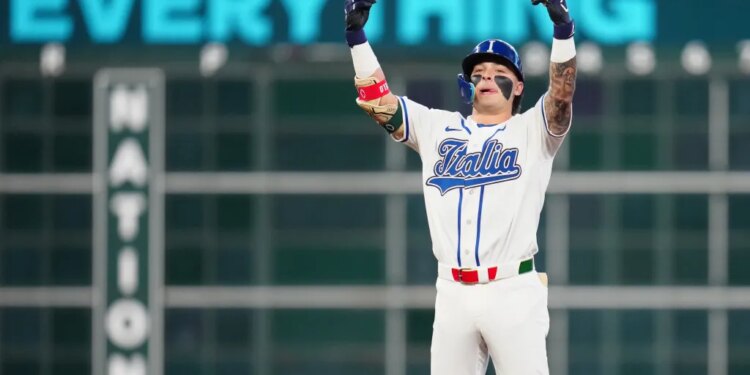 Andrew Fischer in an "Italia" jersey with his arms raised in celebration after hitting a two-run double.