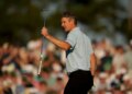 Justin Rose waves to the crowd with a golf club in hand at the Masters golf tournament.
