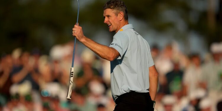 Justin Rose waves to the crowd with a golf club in hand at the Masters golf tournament.