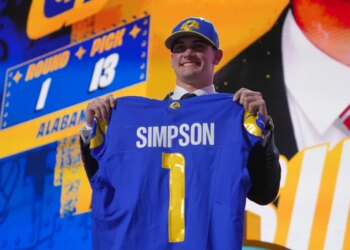 Ty Simpson holds up a blue Los Angeles Rams jersey with his name and number 1 on the back after being drafted.