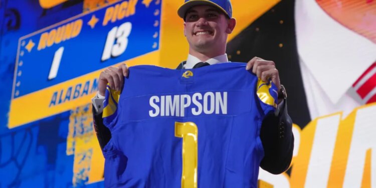 Ty Simpson holds up a blue Los Angeles Rams jersey with his name and number 1 on the back after being drafted.