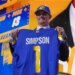 Ty Simpson holds up a blue Los Angeles Rams jersey with his name and number 1 on the back after being drafted.
