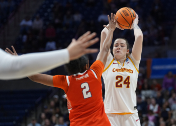 An Iowa State player in a white and gold jersey shoots a basketball while a Syracuse player in an orange jersey defends.