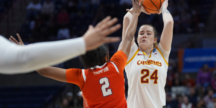 An Iowa State player in a white and gold jersey shoots a basketball while a Syracuse player in an orange jersey defends.