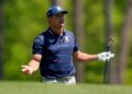 Bryson DeChambeau looking distressed while holding a golf club on a green course.