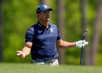Bryson DeChambeau looking distressed while holding a golf club on a green course.