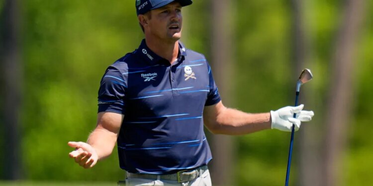 Bryson DeChambeau looking distressed while holding a golf club on a green course.