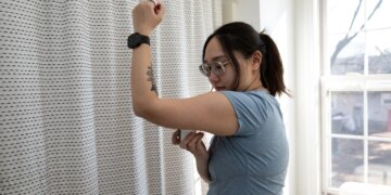 Senior reviewer Victoria Song applying a CGM to the bottom fo her arm in front of a curtain