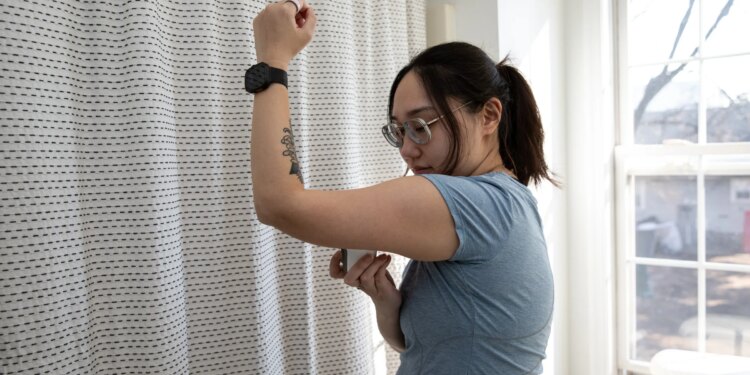 Senior reviewer Victoria Song applying a CGM to the bottom fo her arm in front of a curtain