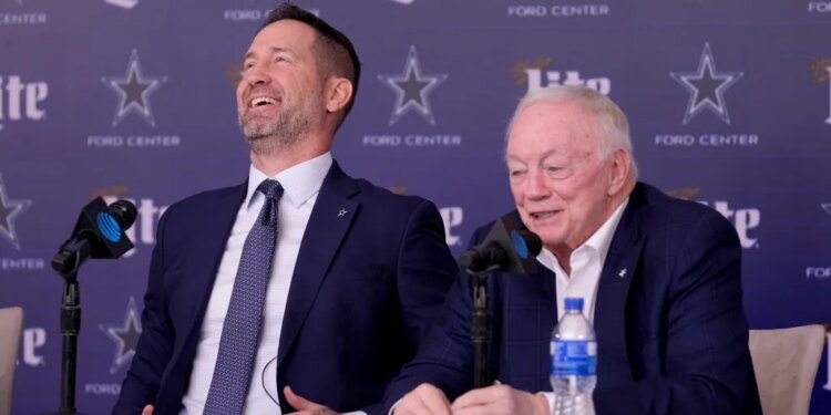 Brian Schottenheimer laughing as Jerry Jones responds to a question at a press conference.
