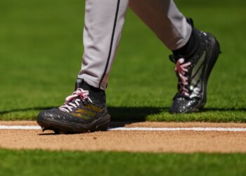 Baseball player Brandon Pfaadt walks on the field, showing his black and gold cleats with pink laces.