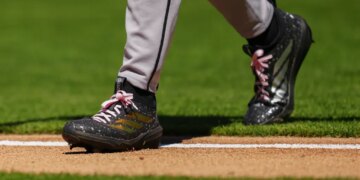 Baseball player Brandon Pfaadt walks on the field, showing his black and gold cleats with pink laces.
