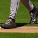 Baseball player Brandon Pfaadt walks on the field, showing his black and gold cleats with pink laces.