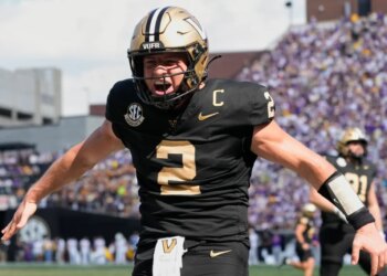 A Vanderbilt football player, wearing number 2, in a black and gold uniform, cheers with his arms outstretched.
