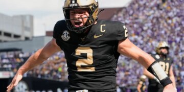 A Vanderbilt football player, wearing number 2, in a black and gold uniform, cheers with his arms outstretched.