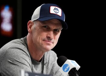 Dan Hurley speaks during a news conference, wearing a blue and white UConn Huskies baseball cap and a grey t-shirt.