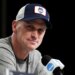 Dan Hurley speaks during a news conference, wearing a blue and white UConn Huskies baseball cap and a grey t-shirt.