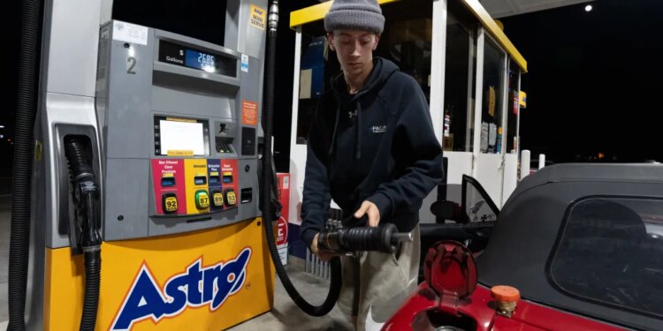 A person in a gray beanie and a black hoodie filling the tank of their red Mazda Miata at an Astro gas station.
