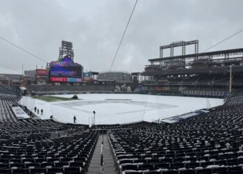 Snow-covered baseball field with visible stadium seats and large screens under a cloudy sky.