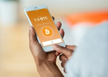 Person holding a smartphone displaying a Bitcoin transaction with "Send 1.5 BTC" and a "Confirm" button.