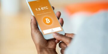 Person holding a smartphone displaying a Bitcoin transaction with "Send 1.5 BTC" and a "Confirm" button.