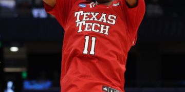 A Texas Tech basketball player in a red jersey with number 11 shoots a basketball.