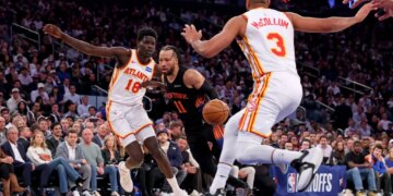 New York Knicks guard Jalen Brunson #11 drives to the basket between Atlanta Hawks forward Mouhamed Gueye #18 and Atlanta Hawks guard CJ McCollum #3.