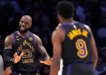 LeBron James in a Lakers uniform with his hands up, facing Bronny James, whose back is to the camera.
